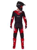 Alpinestars 2025 Racer Veil broek, motorcross broek, zwart en felrood, gedragen als onderdeel van een complete race-uitrusting met bijpassende jersey, zwarte helm, rode crossbril en rode laarzen, met opvallende witte Alpinestars-logo's en sportief ontwerp voor off-road prestaties.