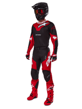 Alpinestars 2025 Racer Veil broek, motorcross broek, zwart en felrood, gedragen als onderdeel van een complete race-uitrusting met bijpassende jersey, zwarte helm, rode bril en rode laarzen, gecoördineerde outfit voor off-road prestaties.