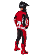Alpinestars 2025 Racer Veil Gear Set, motocrossrijder van achteren gezien in een rood shirt met zwarte panelen en witte logo's, bijpassende rode en zwarte broek met grote witte merklogo's, rode laarzen en een zwarte helm, complete off-road race-outfit
