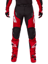 Alpinestars 2025 Racer Veil broek, motorcrossbroek, zwart en felrood, gedragen met bijpassende rode handschoenen en laarzen, voorzien van grote witte Alpinestars-logo's op de dijbenen, zwarte kniepanelen en een verstelbare gespsluiting voor off-road rijden