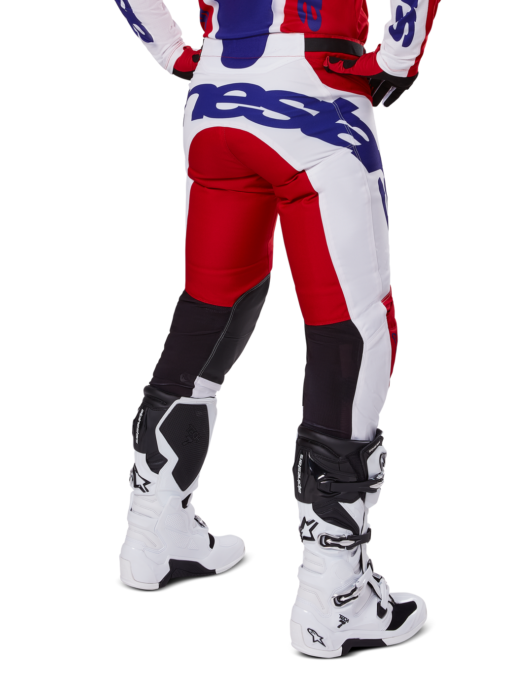 Alpinestars 2025 Racer Veil Pants, motorcrossbroek, helderrood en wit met blauwe branding, achteraanzicht met zwarte stretch ventilatiepanelen op de achterkant van de benen, gecombineerd met witte motorcrosslaarzen.