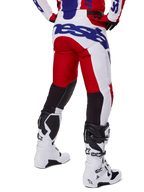 Alpinestars 2025 Racer Veil Pants, motorcrossbroek, helderrood en wit met blauwe branding, achteraanzicht met zwarte stretch ventilatiepanelen op de achterkant van de benen, gecombineerd met witte motorcrosslaarzen.