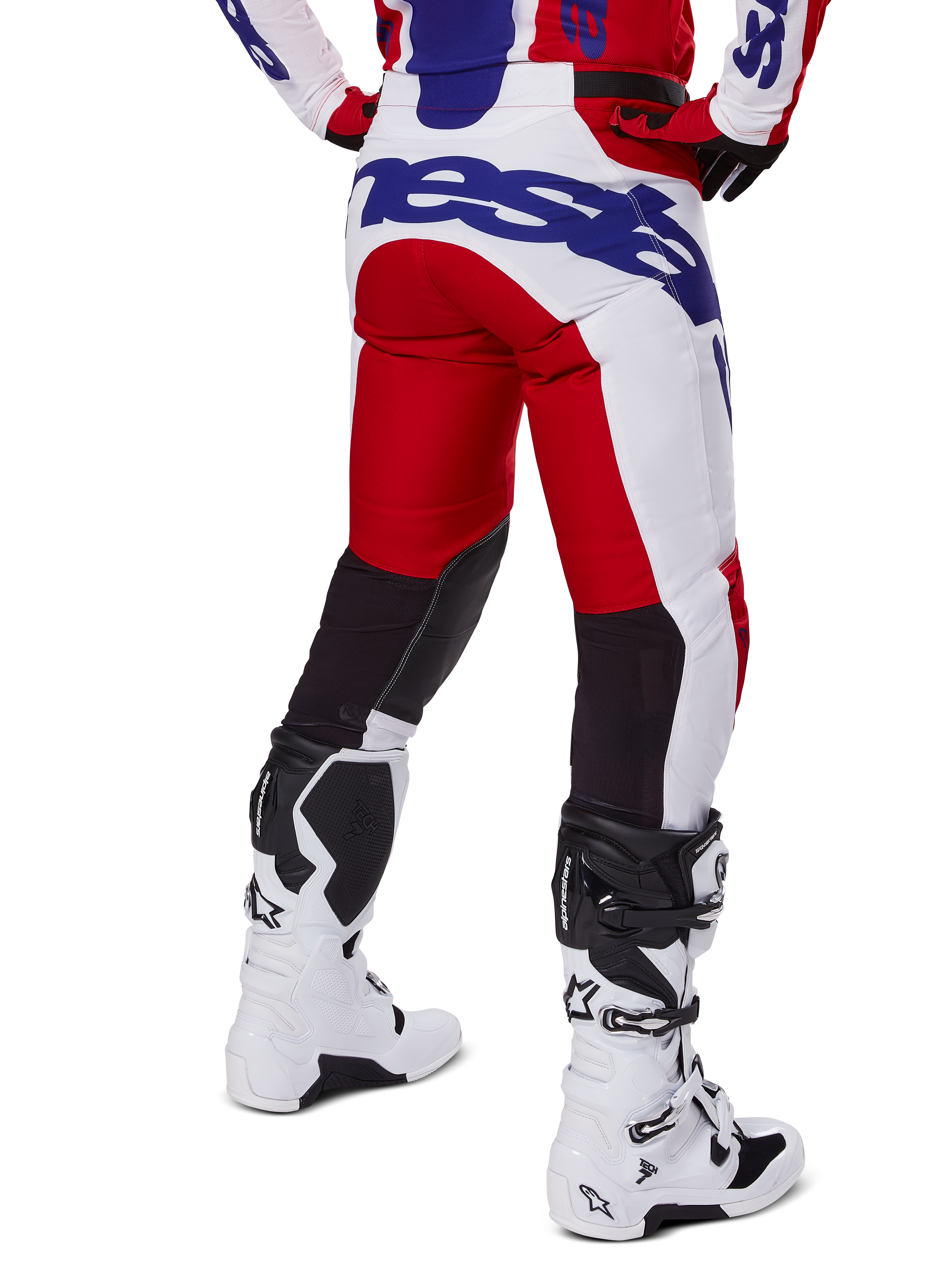 Alpinestars 2025 Racer Veil Pants, motorcrossbroek, helderrood en wit met blauwe branding, achteraanzicht met zwarte stretch ventilatiepanelen op de achterkant van de benen, gecombineerd met witte motorcrosslaarzen.
