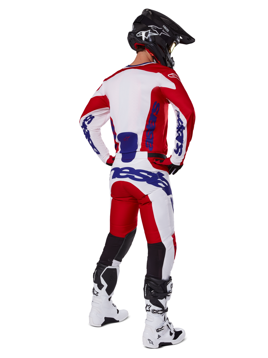 Alpinestars 2025 Racer Veil Pants, motorcrossbroek, felrood en wit met blauwe accenten, van achteren getoond op een rijder in volledige uitrusting, met opvallende Alpinestars-branding, ademende panelen op de onderbenen en bijpassende witte laarzen en een zwarte helm.