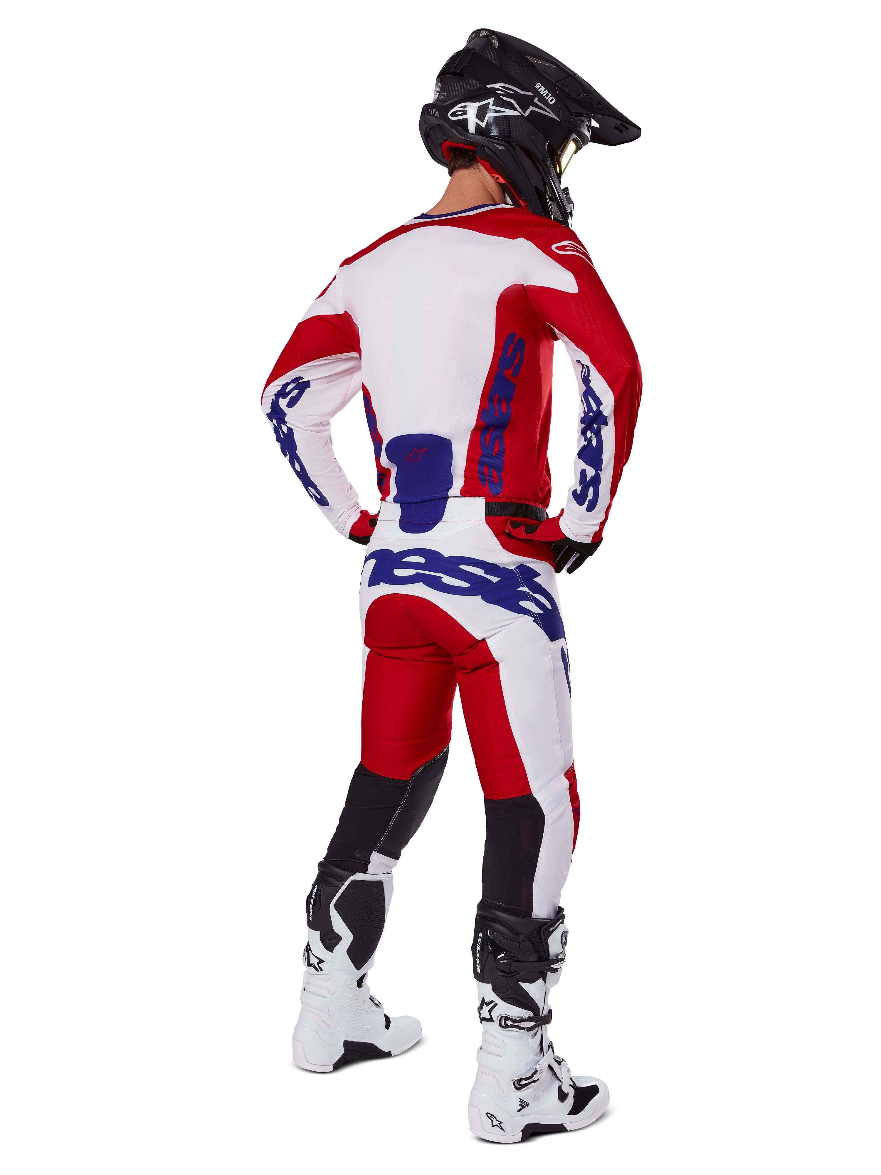 Alpinestars 2025 Racer Veil Pants, motorcrossbroek, felrood en wit met blauwe accenten, van achteren getoond op een rijder in volledige uitrusting, met opvallende Alpinestars-branding, ademende panelen op de onderbenen en bijpassende witte laarzen en een zwarte helm.