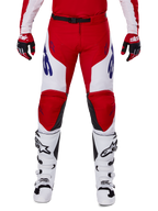 Alpinestars Racer Veil Pants 2025, motorcrossbroek, helderrood en wit, gedragen met bijpassende rode handschoenen en witte laarzen, met blauwe merkdetails op de dijen en een zwarte tailleriem, ergonomische sportieve snit voor prestatiegericht rijden
