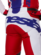 Alpinestars 2025 Racer Veil Pants, motorcrossbroek, felrood en wit met blauwe branding, detail van de achterkant van het zitvlak met een groot Alpinestars-logo, gedragen als onderdeel van een gecoördineerde off-road race-outfit