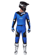 Alpinestars 2025 Racer Veil Pants, motorcrossbroek, blauw en zwart, gedragen als een complete race-outfit met bijpassende blauw-zwarte jersey, zwart-witte helm, blauwe handschoenen en witte laarzen, voorzien van opvallende logo's en een ergonomisch ontwerp voor off-road rijden.