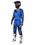 Motocrossrijder in volledige race-uitrusting, met Alpinestars 2025 Racer Veil broek in blauw en zwart, bijpassende blauwe jersey met witte accenten, zwarte helm met witte crossbril, witte en zwarte laarzen en blauwe handschoenen, gecoördineerde outfit voor off-road racing