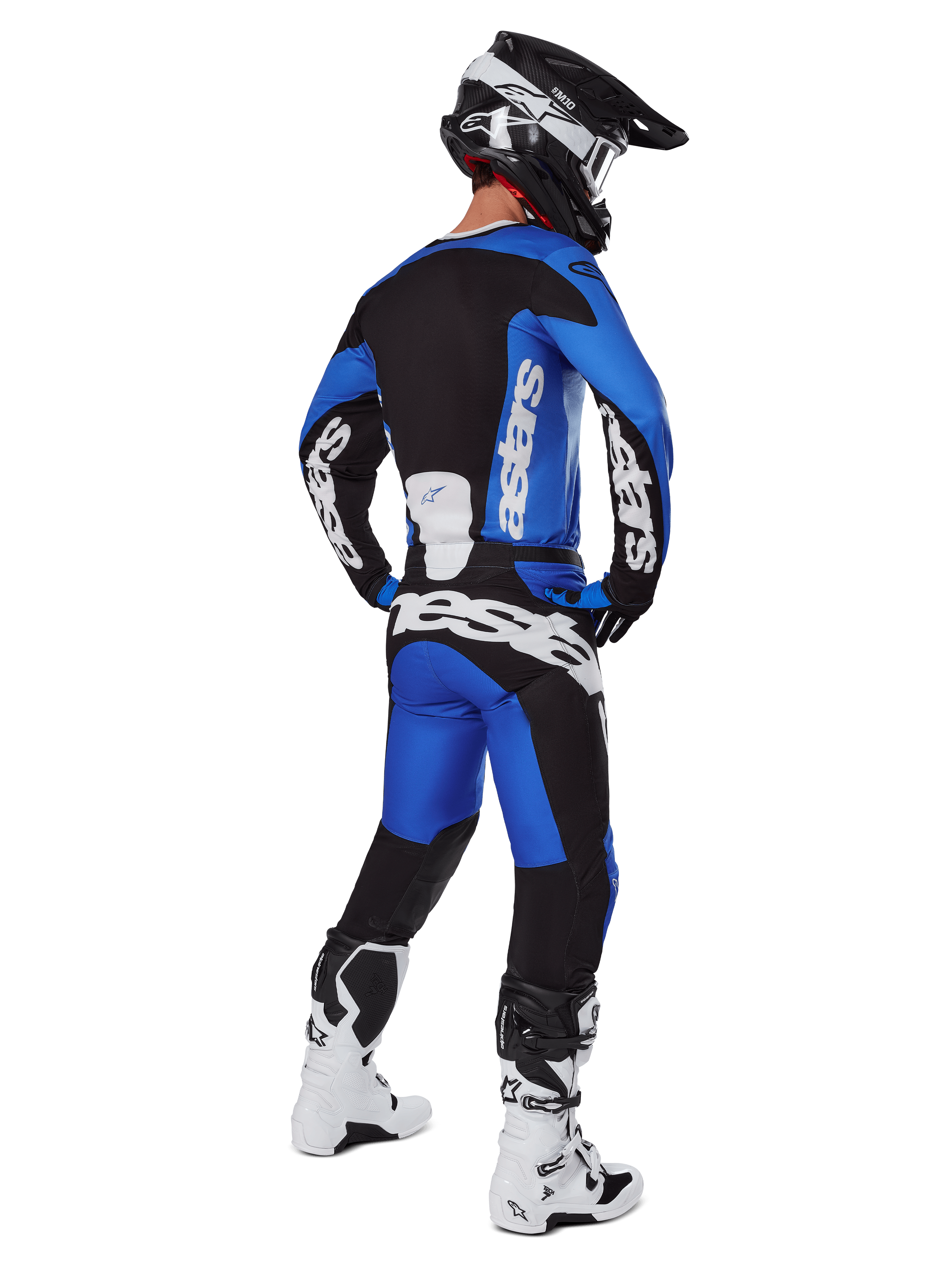 Motorcrossrijder van achteren gezien in Alpinestars 2025 Racer Veil broek in blauw en zwart, bijpassende jersey met lange mouwen en witte branding, witte en zwarte Tech 7 laarzen en een zwarte SM10 helm, volledige off-road race-uitrusting