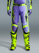 Alpinestars 2026 Racer Portl Pants, motorcrossbroek, paars en fluo geel, gedragen met bijpassende fluo gele laarzen en paarse handschoenen, voorzien van grote sterlogo's en een duurzame polyfabric constructie voor off-road racing