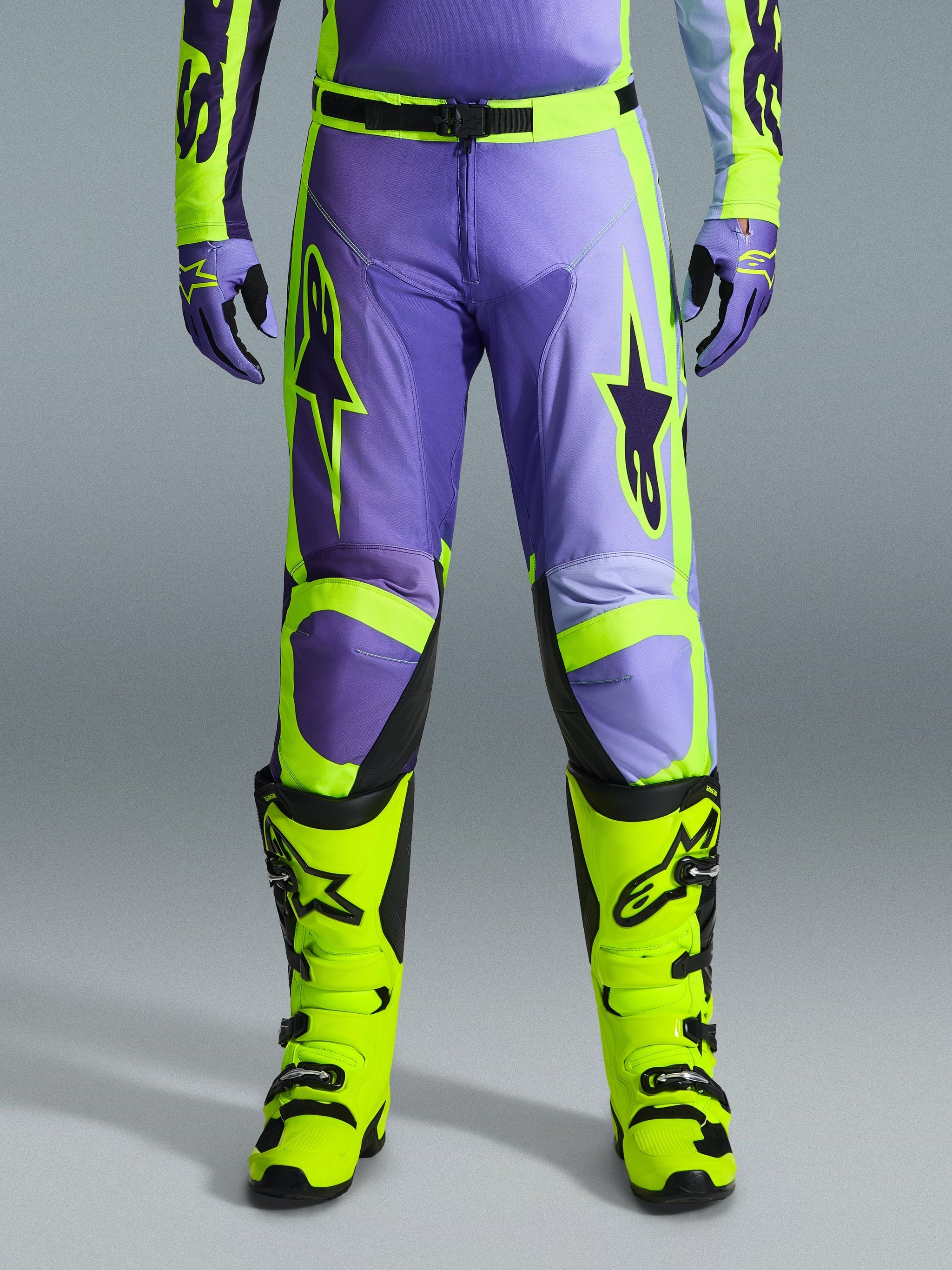 Alpinestars 2026 Racer Portl Pants, motorcrossbroek, paars en fluo geel, gedragen met bijpassende fluo gele laarzen en paarse handschoenen, voorzien van grote sterlogo's en een duurzame polyfabric constructie voor off-road racing