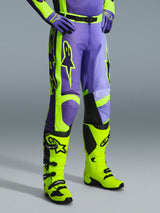 Alpinestars 2026 Racer Portl Pants, motorcrossbroek in paars en fluogeel, gedragen door een rijder met bijpassende fluogele laarzen en paarse handschoenen, met opvallende Alpinestars-branding en ergonomisch ontwerp voor off-road prestaties