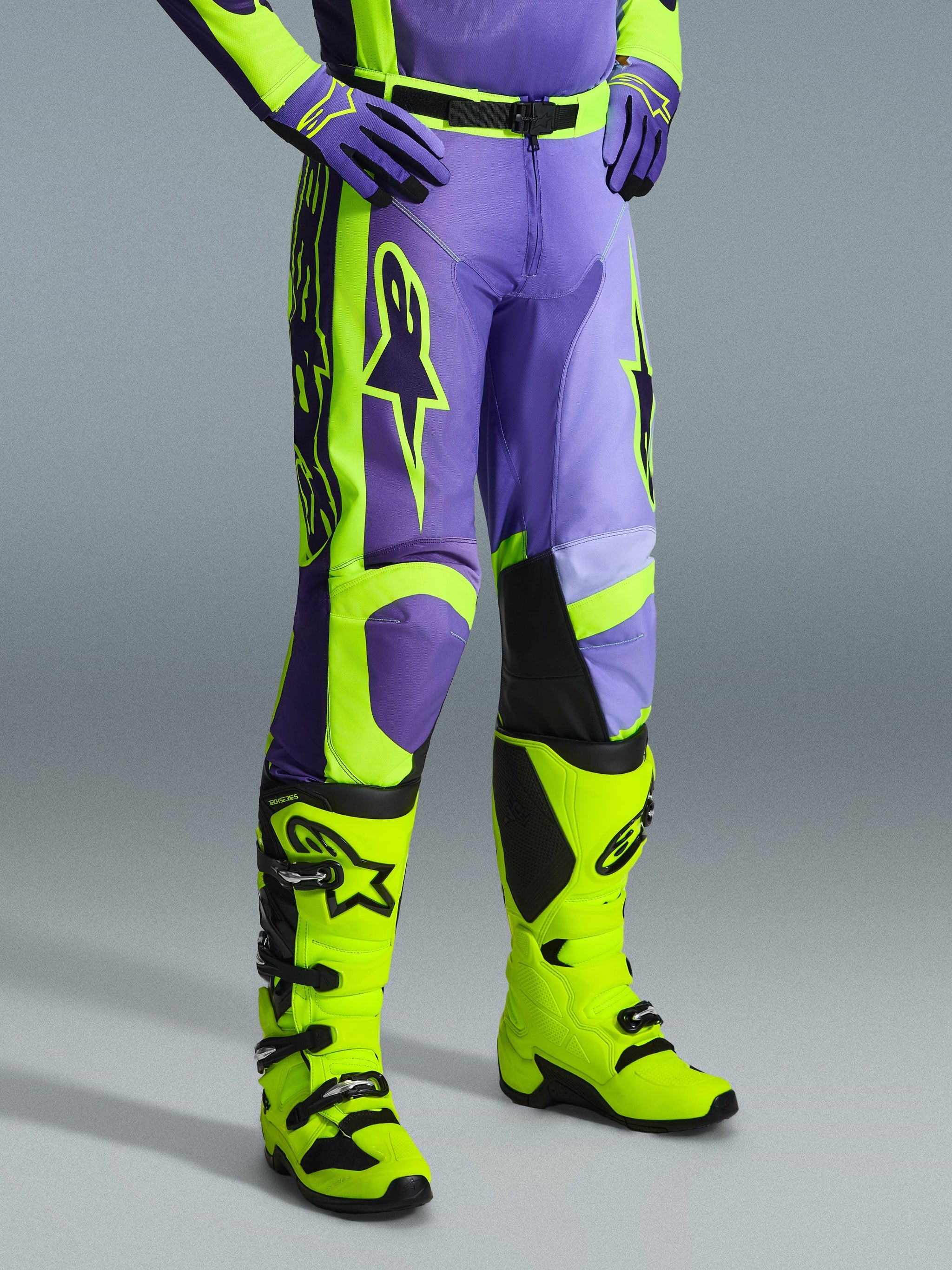 Alpinestars 2026 Racer Portl Pants, motorcrossbroek in paars en fluogeel, gedragen door een rijder met bijpassende fluogele laarzen en paarse handschoenen, met opvallende Alpinestars-branding en ergonomisch ontwerp voor off-road prestaties