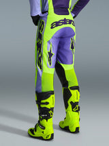 Alpinestars 2026 Racer Portl Broek, motorcrossbroek, paars en neon geel, achteraanzicht met opvallende astars-branding en paarse accenten, gedragen met bijpassende neon gele motorcrosslaarzen, duurzaam synthetisch materiaal voor off-road racing