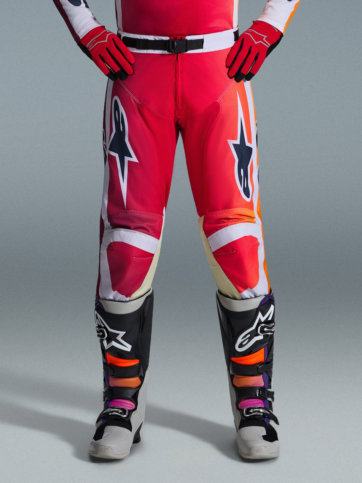 Alpinestars 2026 Racer Portl broek, motorcrossbroek, rood lichtgrijs en donkergrijs, gedragen met bijpassende rode handschoenen en veelkleurige laarzen, met opvallende Alpinestars-sterlogo's op de dijen en witte accenten, sportief ontwerp voor off-road racen