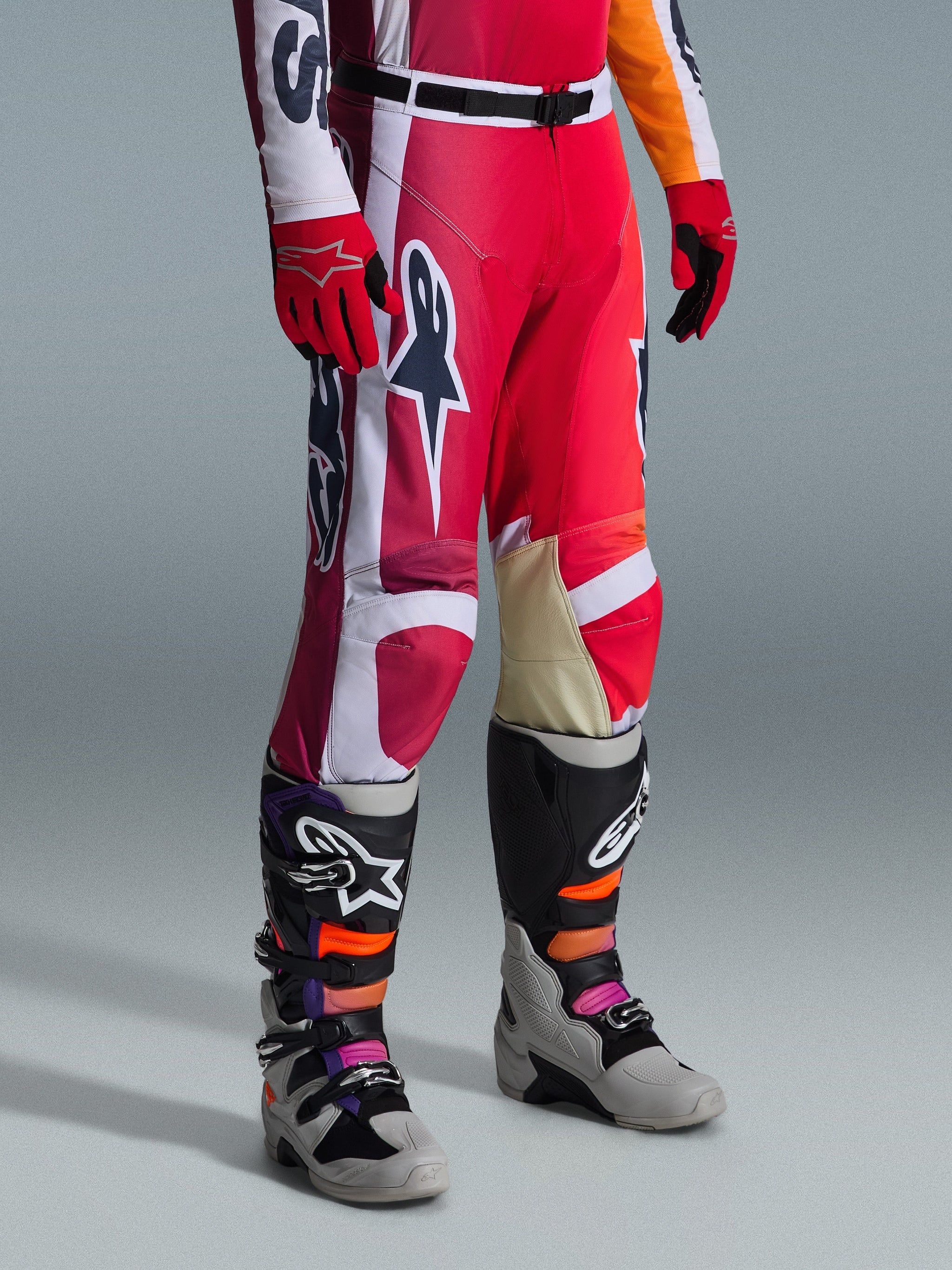 Alpinestars Racer Portl broek 2026, motorcrossbroek, rood, lichtgrijs en donkergrijs, gedragen met bijpassende rode handschoenen en veelkleurige motorcrosslaarzen, voorzien van opvallende Alpinestars-logo's en verstevigde panelen voor off-road racen.
