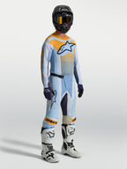 Alpinestars Techstar Maven heren-motocrossbroek, blauw en oranje, met bijpassende jersey, witte motorlaarzen en zwarte helm.