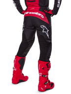 Alpinestars 2025 Fluid Haul Gear Set, achteraanzicht, zwarte en rode motorcrossbroek met grote witte logo's, bijpassende jersey en felrode Tech 7 laarzen, gecoördineerde off-road race-uitrusting