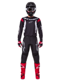 Alpinestars 2025 Fluid Haul Gearset, motorcrosser in volledige race-uitrusting, zwart jersey met rode schouderaccenten en witte logo's, zwarte broek met witte ster-branding, felrode laarzen, rood-zwarte handschoenen, zwarte helm met witte crossbril, op elkaar afgestemde off-road performance-look