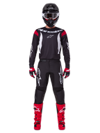 Alpinestars 2025 Fluid Haul Gearset, motorcrosser in volledige race-uitrusting, zwart jersey met rode schouderaccenten en witte logo's, zwarte broek met witte ster-branding, felrode laarzen, rood-zwarte handschoenen, zwarte helm met witte crossbril, op elkaar afgestemde off-road performance-look