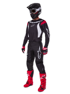 Motocross-rijder in een complete Alpinestars 2025 Fluid Haul gearset, zwart jersey met rode en witte accenten, zwarte broek met witte logo's, felrode laarzen, rood-zwarte handschoenen, zwarte helm met crossbril, gecoördineerde off-road prestatiegerichte uitrusting