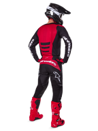 Motorcrossrijder die de Alpinestars 2025 Fluid Haul Gear Set draagt, achteraanzicht, rood en zwart jersey met witte branding, bijpassende zwarte broek met rode accenten, felrode laarzen en zwarte helm met witte crossbril, complete gecoördineerde outfit voor off-road racen