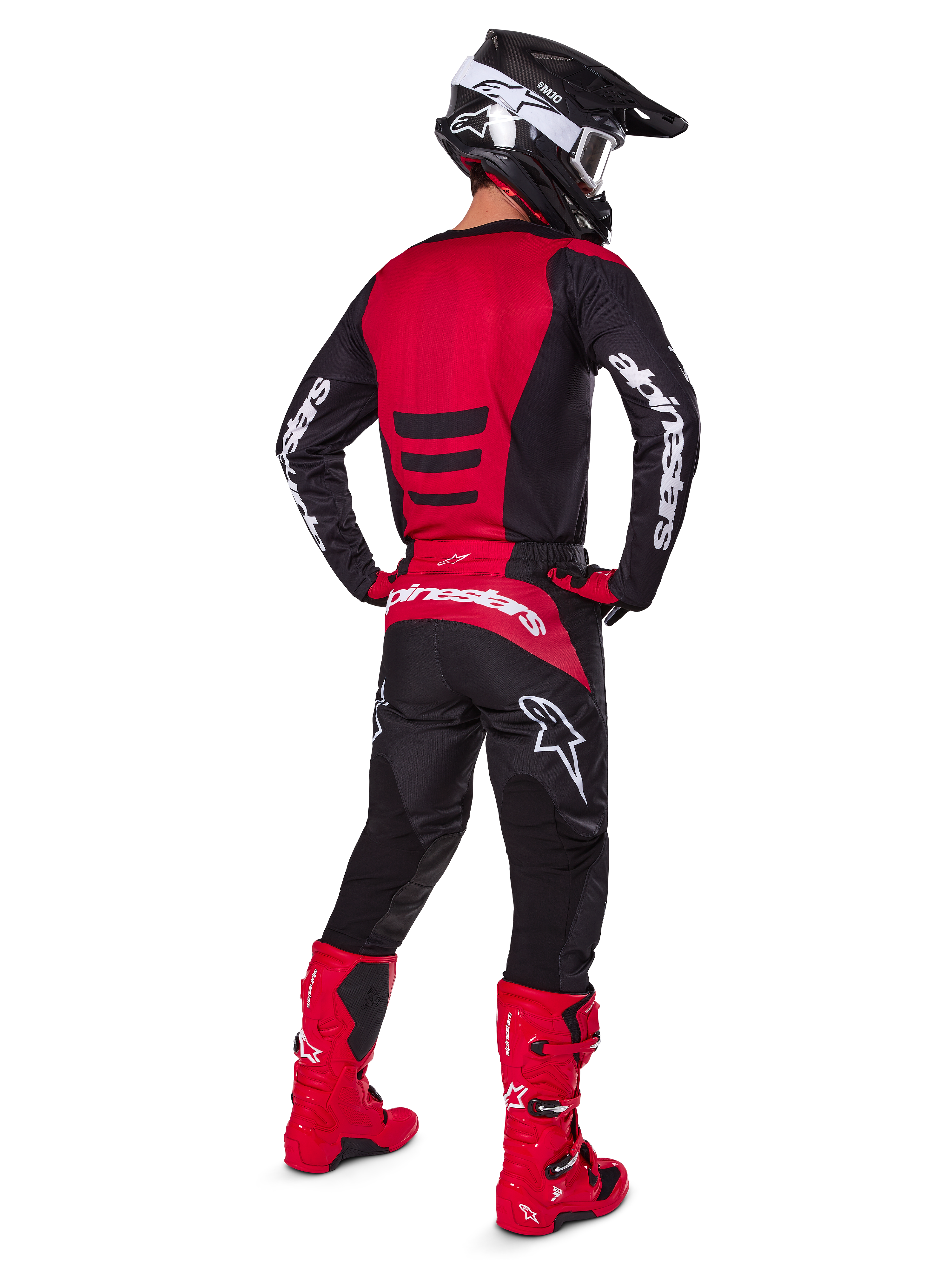 Motorcrossrijder die de Alpinestars 2025 Fluid Haul Gear Set draagt, achteraanzicht, rood en zwart jersey met witte branding, bijpassende zwarte broek met rode accenten, felrode laarzen en zwarte helm met witte crossbril, complete gecoördineerde outfit voor off-road racen