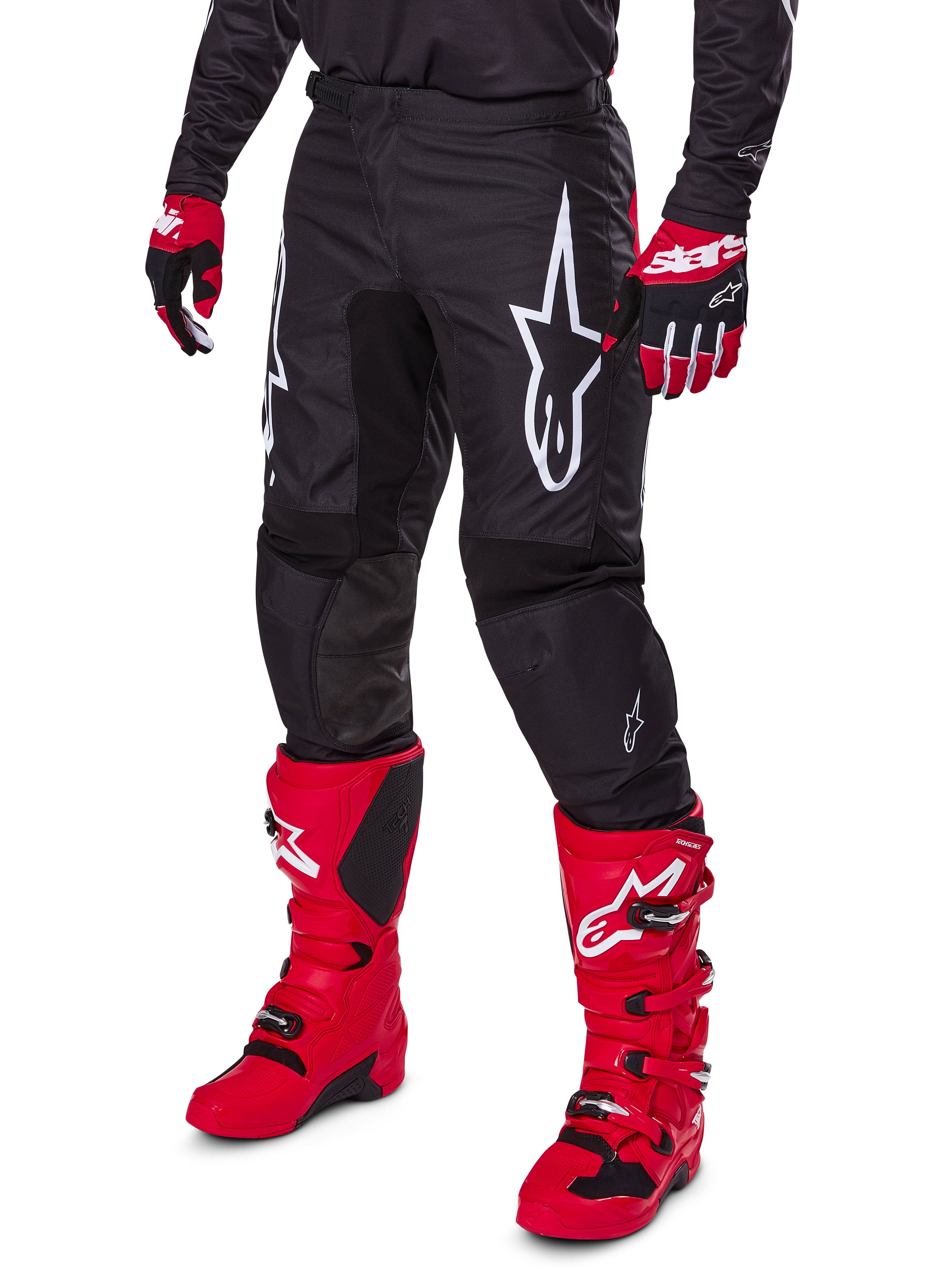 Alpinestars 2025 Fluid Haul broek, motorcrossbroek, zwart, voorzien van een groot wit Alpinestars-logo, gedragen met felrode laarzen en rood-zwarte handschoenen, duurzame 600D polyfabric constructie met ergonomische snit voor off-road racing