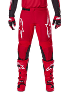 Alpinestars 2025 Fluid Haul broek, motorcrossbroek, felrood en zwart, met grote witte logo's op de dijen en zwarte panelen aan de binnenkant van de benen, gedragen met bijpassende rode laarzen en handschoenen, sportieve pasvorm voor motorcross-prestaties