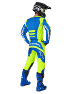 Alpinestars 2025 Fluid Haul broek en bijpassende jersey, motorcrosser van achteren gezien, fluoriserend geel en blauw, gecombineerd met blauwe laarzen en een zwarte Alpinestars helm, professionele off-road race-uitrusting