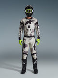 Motocross rider wearing the Alpinestars 2026 Racer Lahnd Gear Set, Sand Camo patterned suit with white, gray, and black design, black helmet with neon green goggles, bright neon green gloves, and black boots with white logos, complete coordinated outfit for off-road racing
