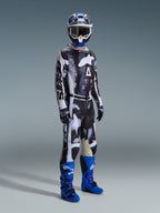 Motocross rider wearing the Alpinestars 2026 Racer Lahnd Jersey and matching pants in Iron Camo, featuring a black and white graphic pattern, paired with blue boots, a blue and white helmet, and black gloves, full racing gear for off-road riding.