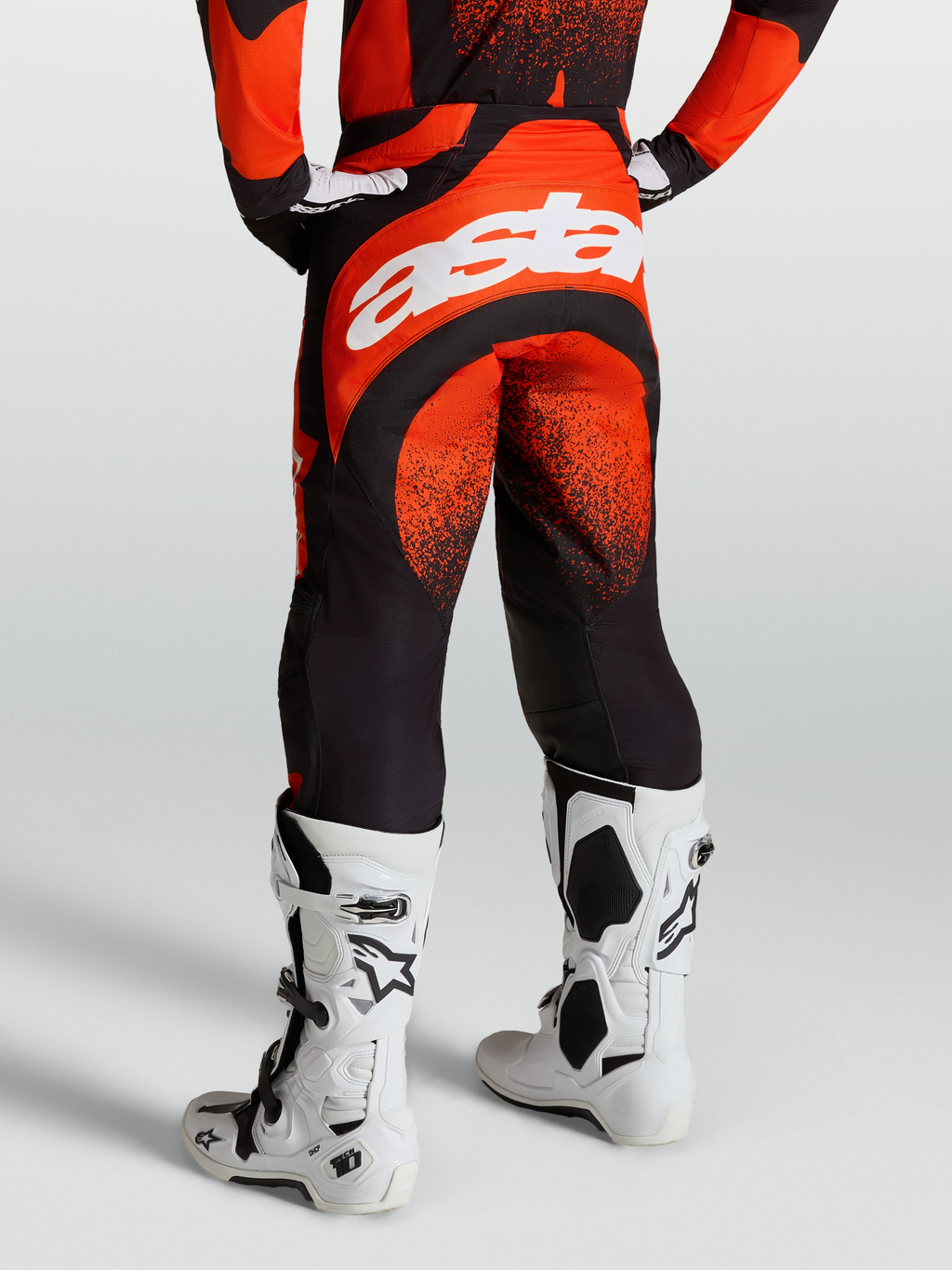 Alpinestars Techstar Swan broek, heren motorcrossbroek, rood en zwart, wit Astar-logo, gedragen met witte Tech 10 laarzen.