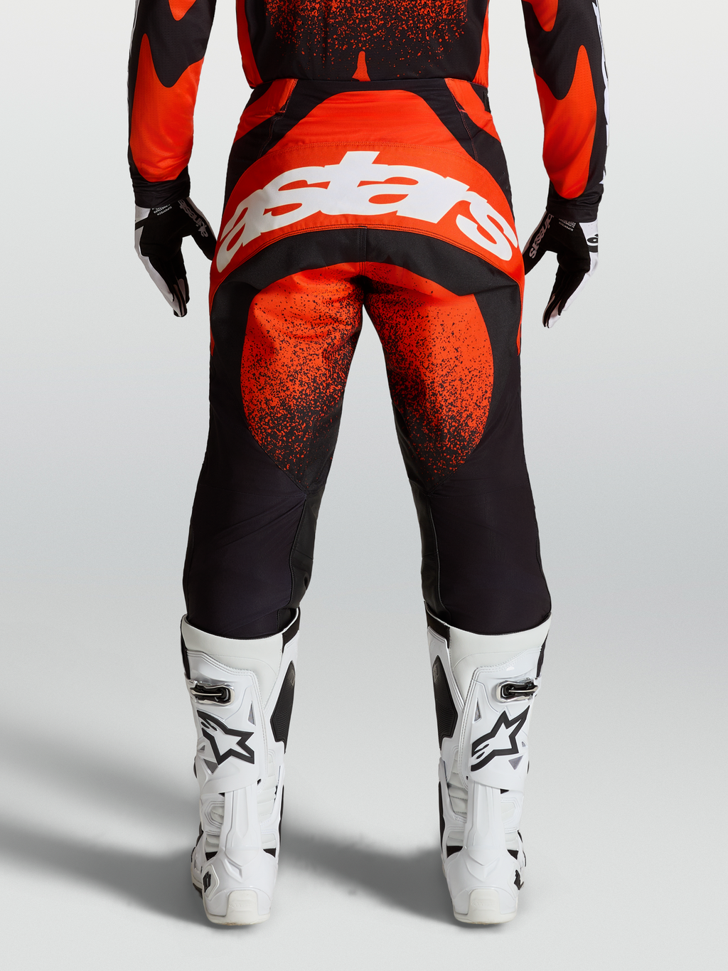 Alpinestars Techstar Swan broek, rode en zwarte motocrossuitrusting, achteraanzicht op model met wit Alpinestars-logo en witte motorlaarzen.