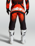 Alpinestars Techstar Swan broek, rode en zwarte motocrossuitrusting, achteraanzicht op model met wit Alpinestars-logo en witte motorlaarzen.