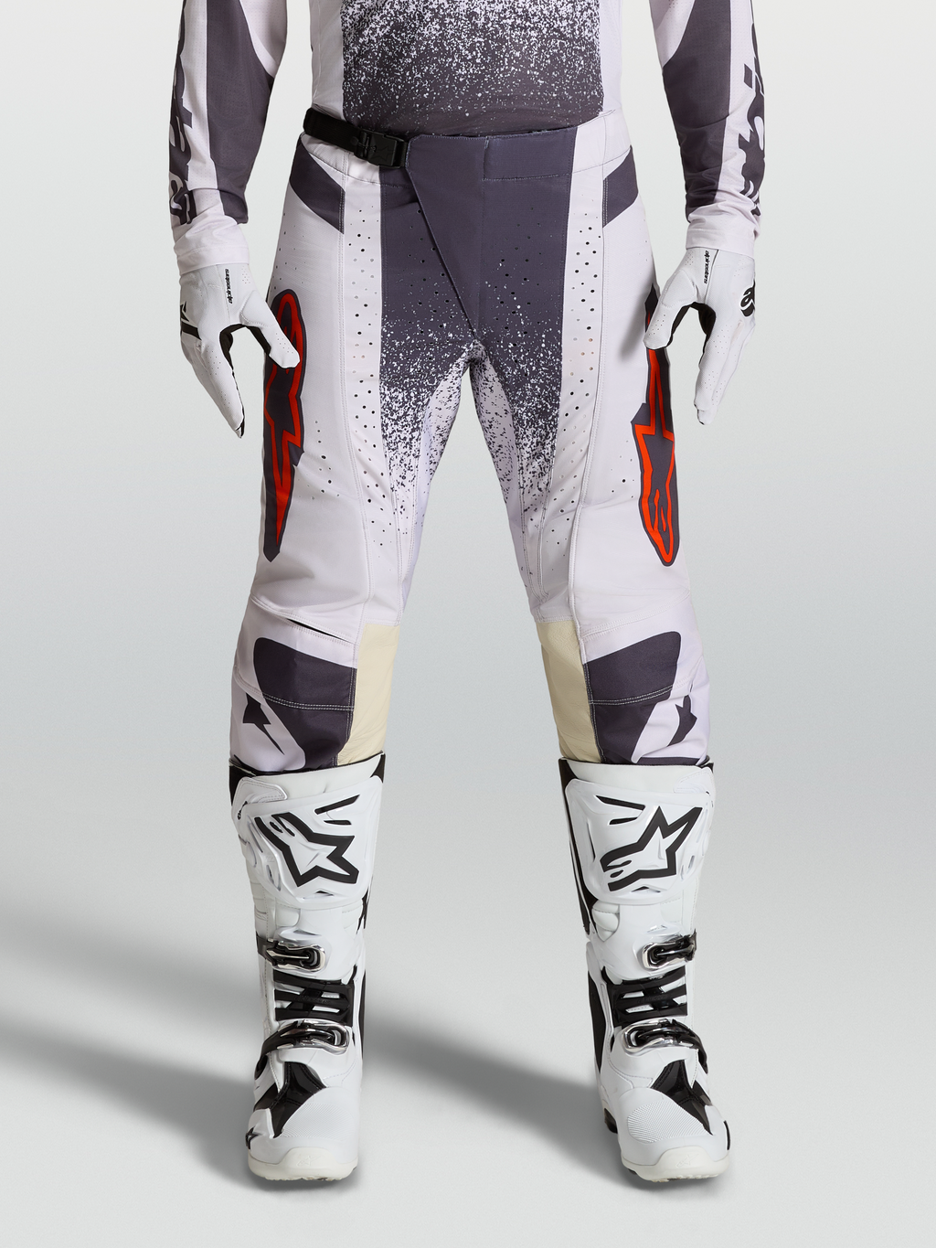 Alpinestars Techstar Swan broek voor motocross, lichtlila en donkergrijs met rode accenten, gedragen met witte laarzen en handschoenen.