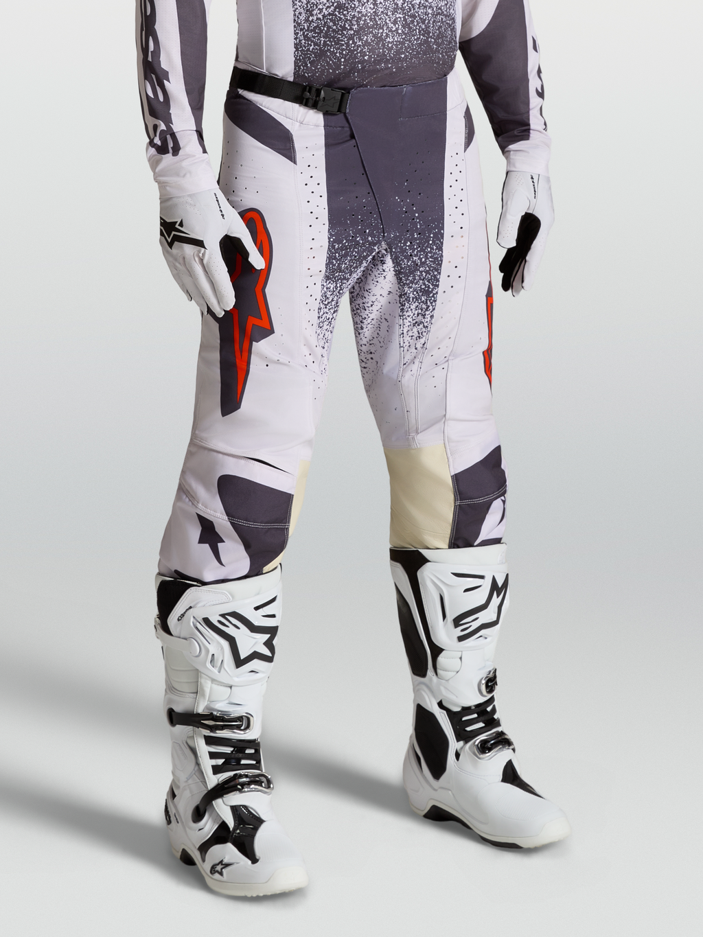 Alpinestars Techstar Swan broek, motocross-racebroek voor heren, licht lila en donkergrijs met rood fluo accenten, on-model foto met handschoenen en laarzen.