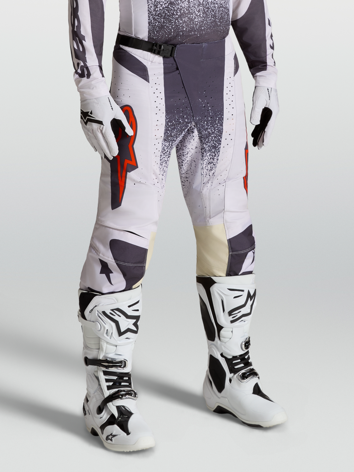 Alpinestars Techstar Swan broek, motocross-racebroek voor heren, licht lila en donkergrijs met rood fluo accenten, on-model foto met handschoenen en laarzen.