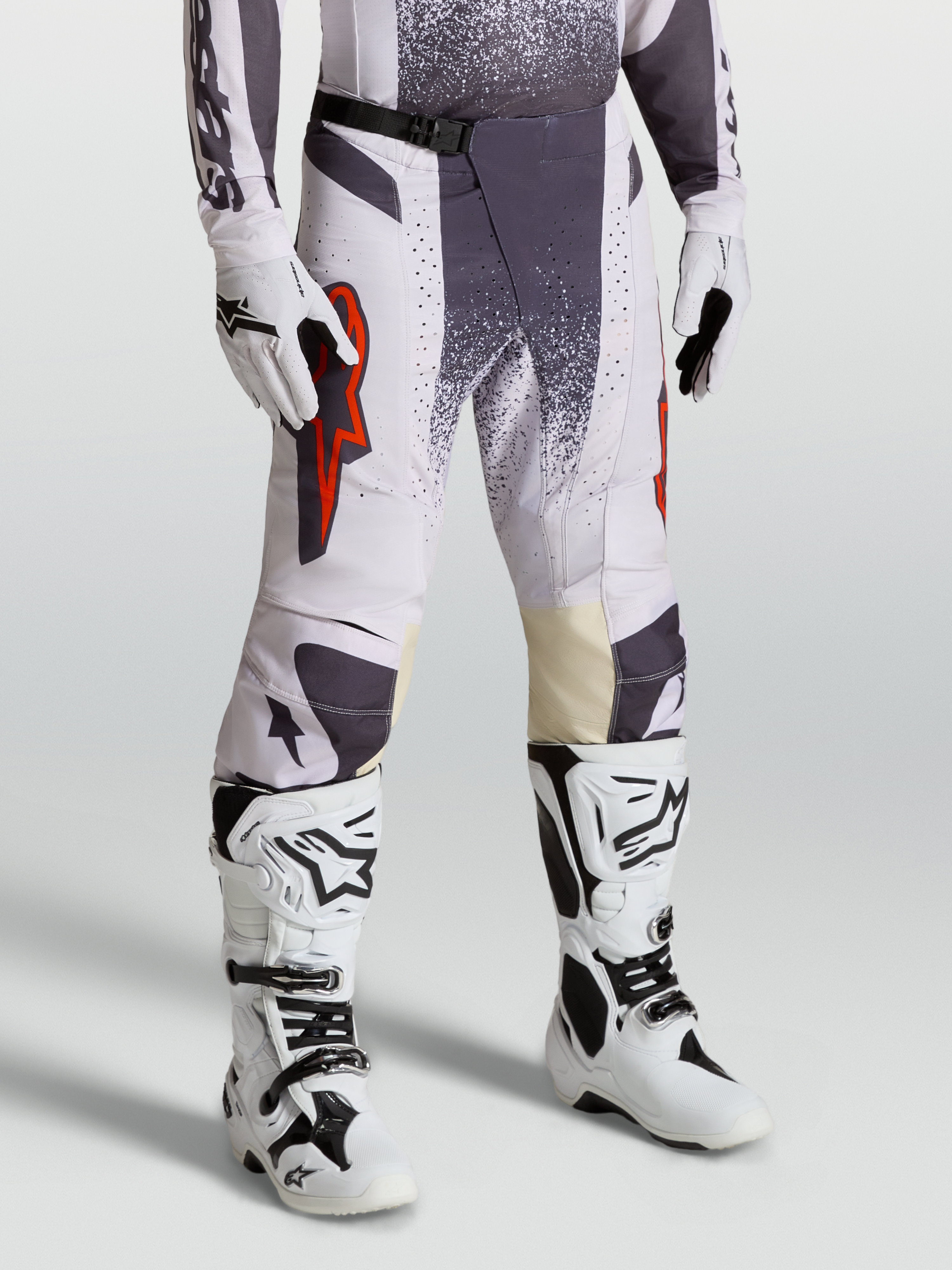 Alpinestars Techstar Swan broek, motocross-racebroek voor heren, licht lila en donkergrijs met rood fluo accenten, on-model foto met handschoenen en laarzen.