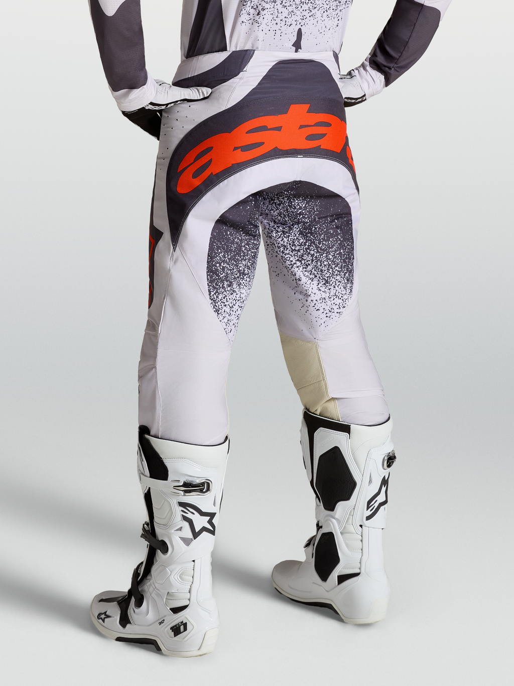 Alpinestars Techstar Swan broek voor heren, motocrossracebroek in licht lila en donkergrijs met rood fluo accenten, gedragen met witte Tech 10 motorlaarzen, professionele off-road motoruitrusting.