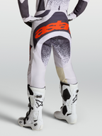 Alpinestars Techstar Swan broek voor heren, motocrossracebroek in licht lila en donkergrijs met rood fluo accenten, gedragen met witte Tech 10 motorlaarzen, professionele off-road motoruitrusting.