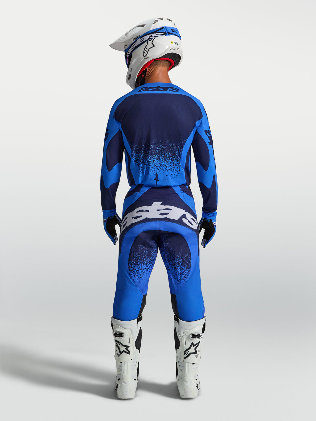 Alpinestars Techstar Swan broek, heren-motocrossbroek in blauw en donkerblauw, achterzijde met witte motorlaarzen.