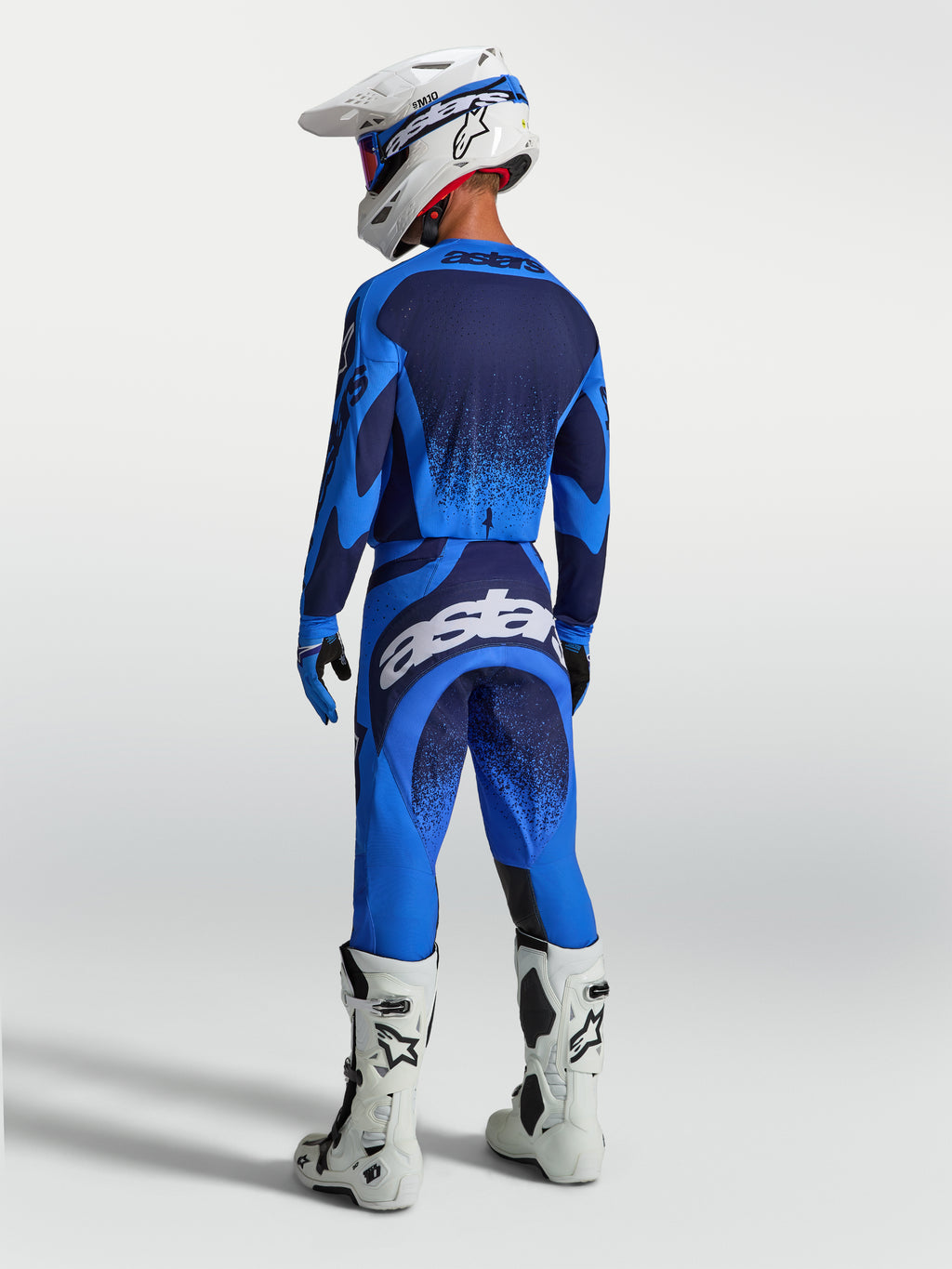 Alpinestars Techstar Swan broek, heren-motocrossbroek in blauw en wit, atletische racepasvorm, van achteren getoond op een model met complete motocross-uitrusting.