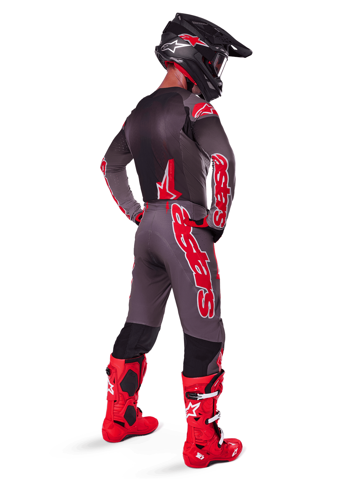 Motorcrosser in Alpinestars 2025 Supertech Lipan Pants, Smoke Bright Red, grijze broek met grote rode logo's en zwarte panelen aan de binnenkant van de benen, gecombineerd met bijpassende grijze jersey, zwarte helm en felrode laarzen, complete off-road race-outfit van achteren gezien.