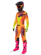 Alpinestars 2025 Supertech Lipan crossbroek, motorcross broek, geel en roze, gedragen als onderdeel van een volledige uitrusting met bijpassende jersey met kleurverloop, felroze laarzen, gele handschoenen en zwarte helm, voorzien van opvallende zwarte logo's en sportieve pasvorm voor off-road racen