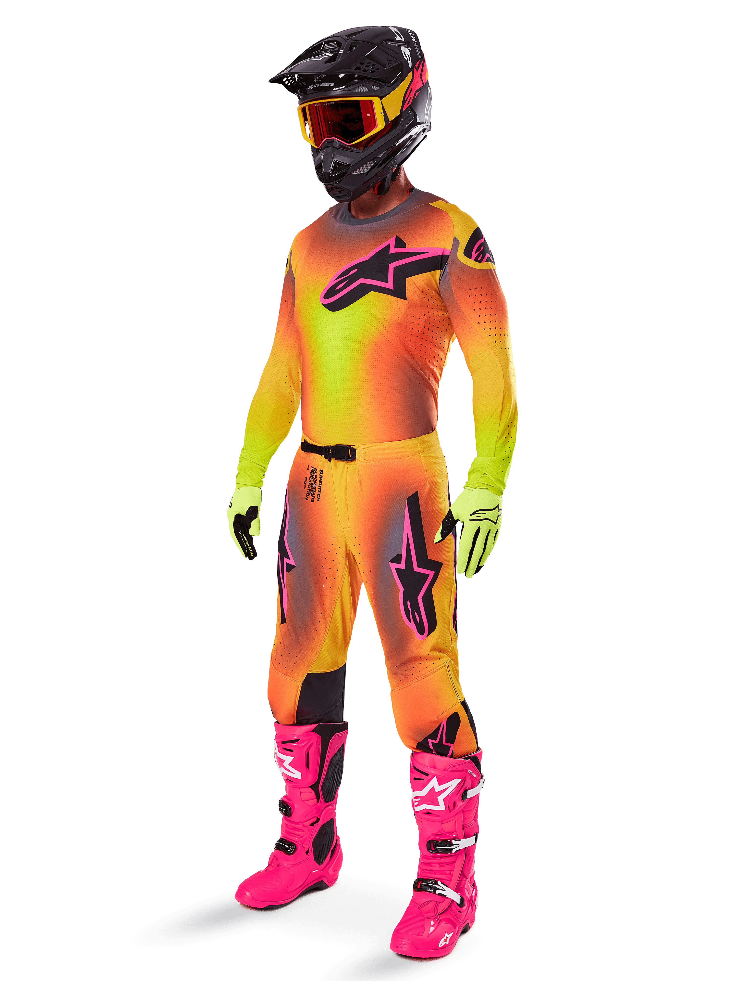 Alpinestars 2025 Supertech Lipan crossbroek, motorcross broek, geel en roze, gedragen als onderdeel van een volledige uitrusting met bijpassende jersey met kleurverloop, felroze laarzen, gele handschoenen en zwarte helm, voorzien van opvallende zwarte logo's en sportieve pasvorm voor off-road racen
