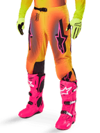 Alpinestars 2025 Supertech Lipan Gear Set, motorcrossbroek, geel en oranje kleurverloop met roze en paarse accenten, zwarte logo's op de dijen, gedragen met gele handschoenen en felroze motorcrosslaarzen