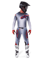 Motocrossrijder in Alpinestars 2025 Supertech Lipan broek en bijpassende jersey in Grijs Oranje Fluo, met opvallende oranje en marineblauwe logo's, gecombineerd met een zwarte helm, rode handschoenen en wit-zwarte laarzen, volledige race-uitrusting voor off-road prestaties.
