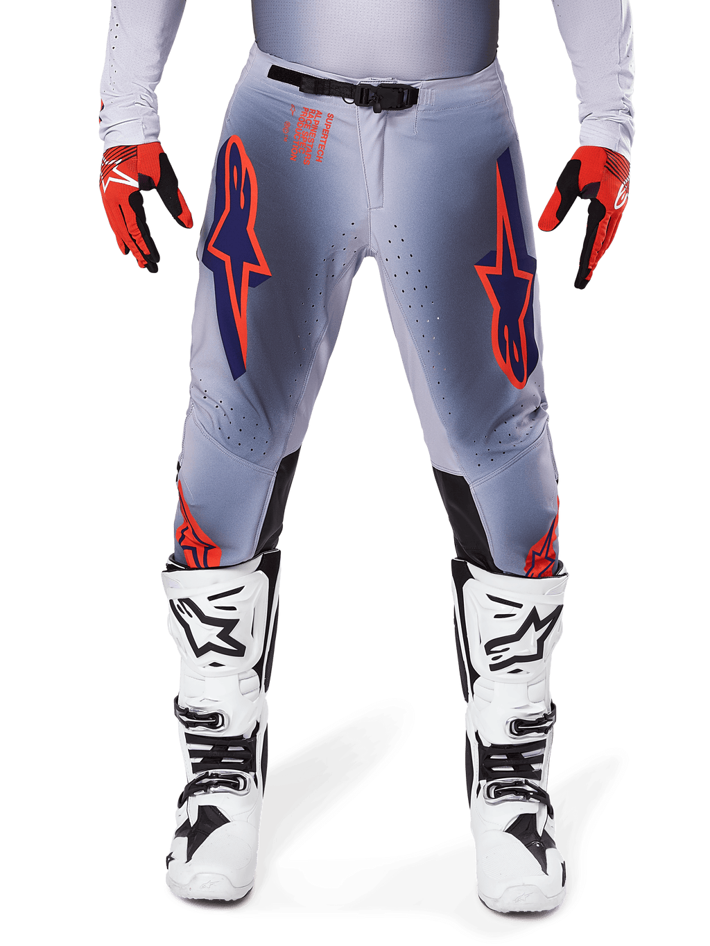 Alpinestars 2025 Supertech Lipan broek, motorcrossbroek, grijs en neonoranje, gedragen met rood-zwarte handschoenen en wit-zwarte laarzen, met grote Alpinestars-sterlogo's op de dijen en ventilatieperforaties voor professioneel racen